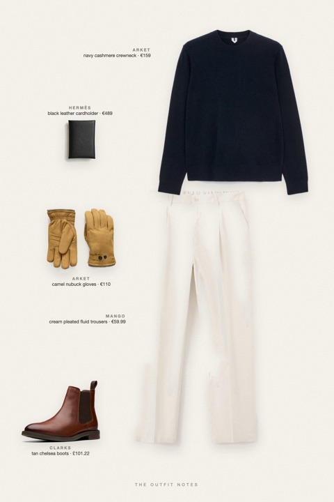 Flat-lay of the pieces in this outfit: navy cashmere crewneck, cream pleated fluid trousers, tan chelsea boots, black leather cardholder, camel nubuck gloves.
