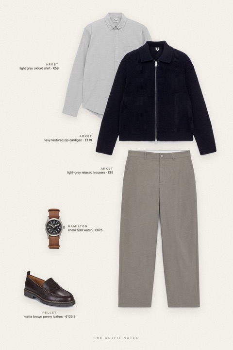 Flat-lay of the pieces in this outfit: navy textured zip cardigan, light grey oxford shirt, light-grey relaxed trousers, matte brown penny loafers, khaki field watch.
